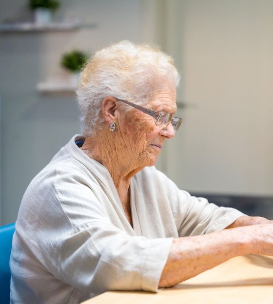 An older woman stacks wooden blocks at a table during a day program activity.