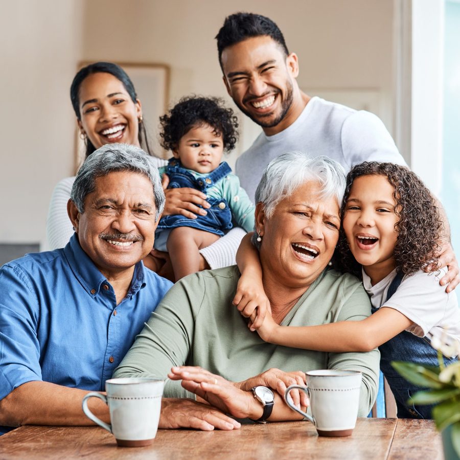 Three generations of a family laugh together around a kitchen table.
