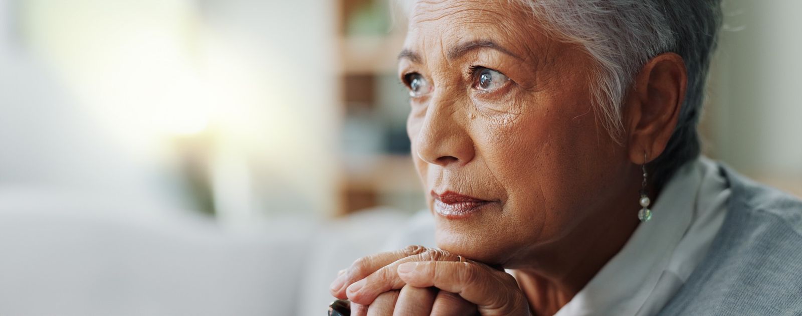 An older woman resting her chin on her hands, looking out a window.