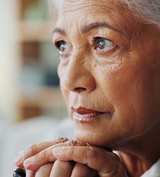 An older woman resting her chin on her hands, deep in thought.